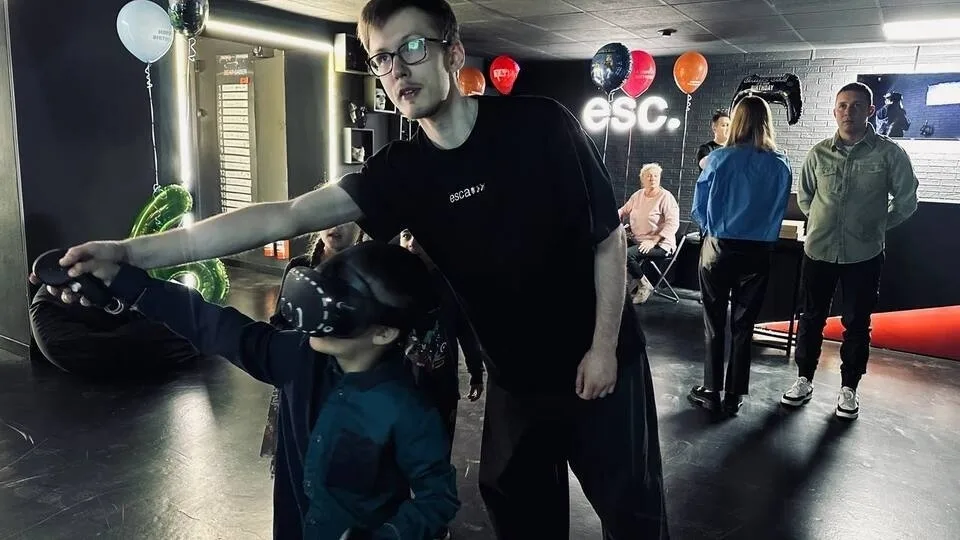 Администратор-ведущий помогает мальчику в VR-шлеме